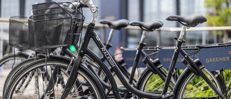 En svart Raleigh-cykel med en korg och en grön lampa som visar om den är påslagen, parkerad framför en byggnad med en skylt som lyder: "Att cykla är miljövänligt".