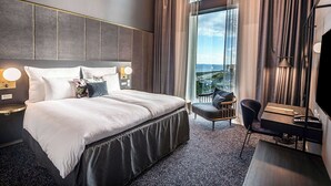 A modern hotel room with a large bed, a desk, and a chair. There is a view of the city through large windows. - Clarion Hotel Copenhagen Airport (Kastrup)