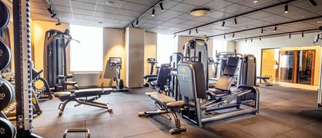 A gym with various exercise machines, a large window, and a door leading to another room.