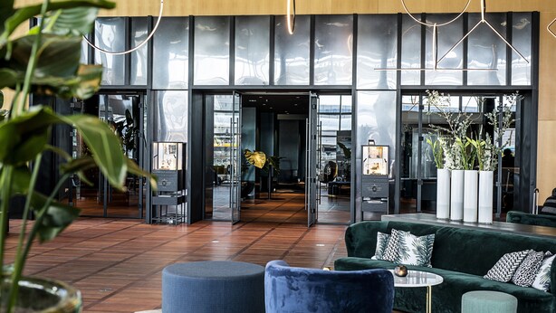 A modern lobby with a green sofa, a round ottoman, and a small table. There are potted plants and a large window with a view. - Clarion Hotel Copenhagen Airport (Kastrup)
