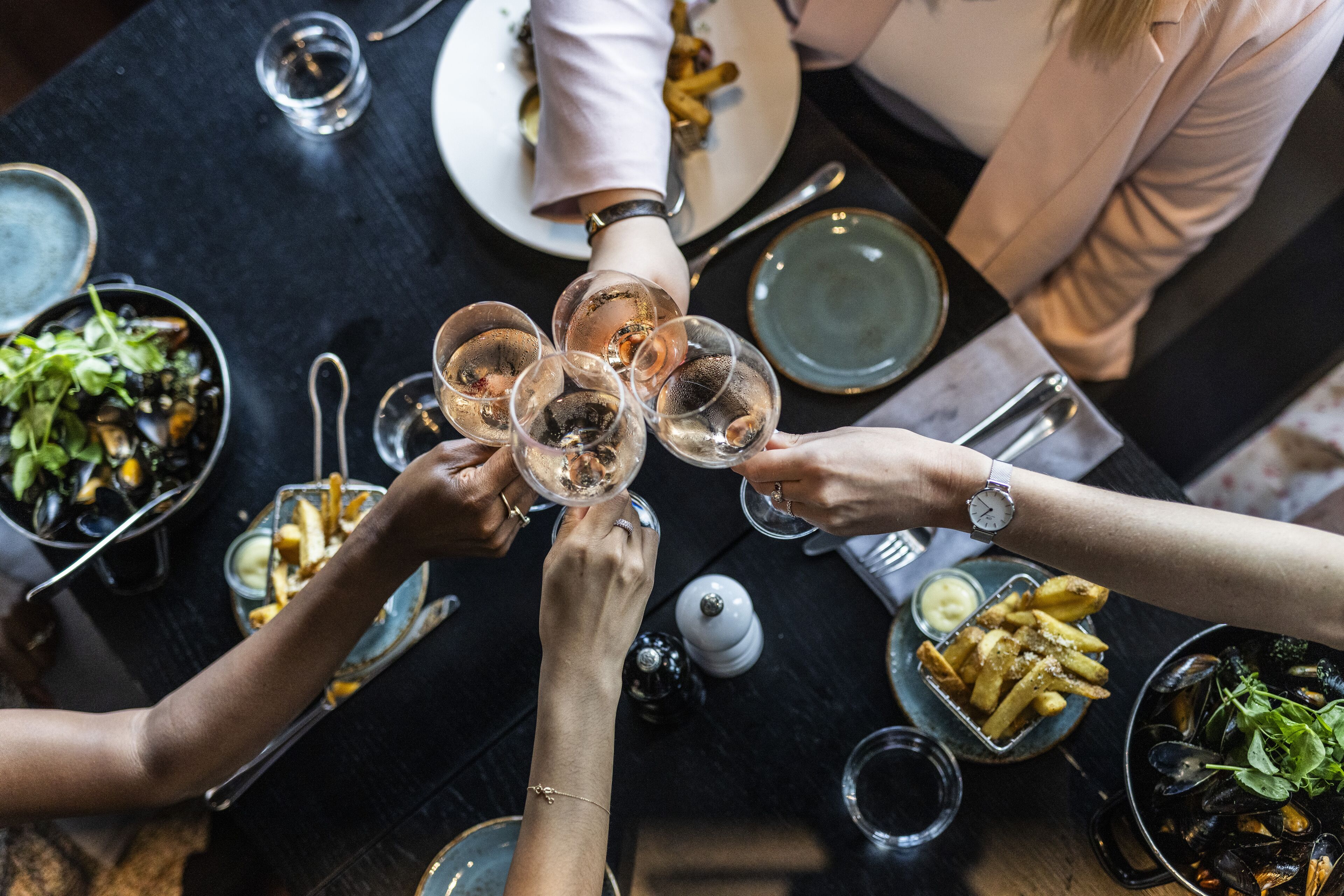Un grupo de personas brindando con copas de vino alrededor de una mesa con comida y bebidas.