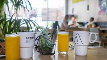 Una mesa con un vaso de jugo de naranja, una taza blanca con diseño geométrico y otra taza blanca con texto.