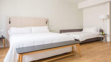 Una habitación de hotel moderna con dos camas, un banco, una mesita de noche, una lámpara y una pequeña mesa con manzanas.