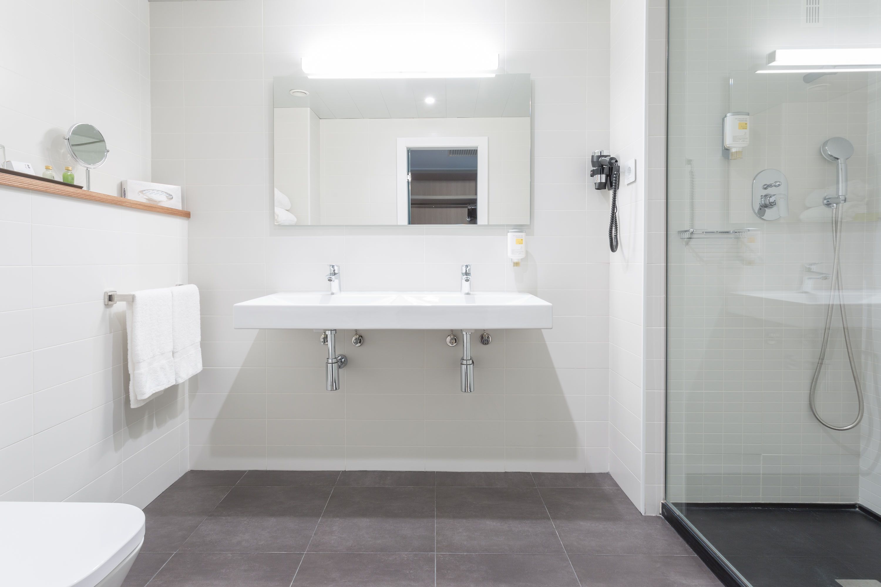 Un baño moderno con un lavabo blanco, dos grifos, un espejo y una cabina de ducha con paredes de vidrio.