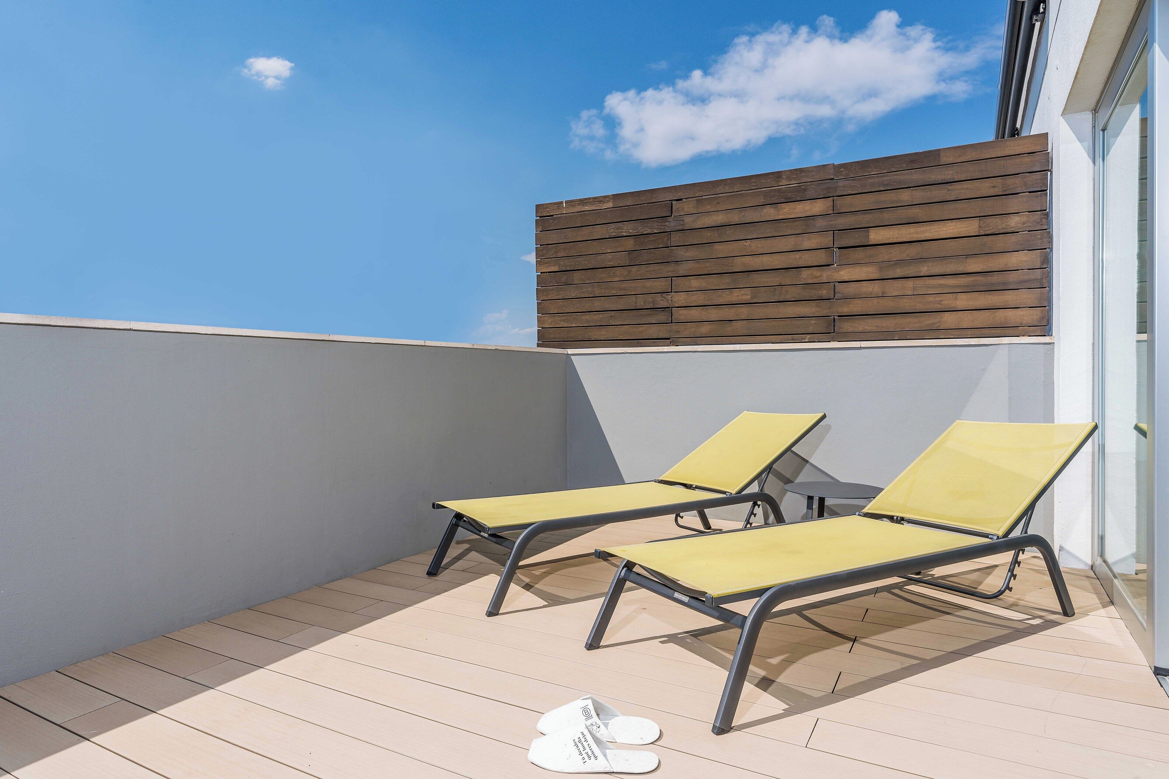 A rooftop terrace with two yellow lounge chairs and a pair of white slippers on the floor.