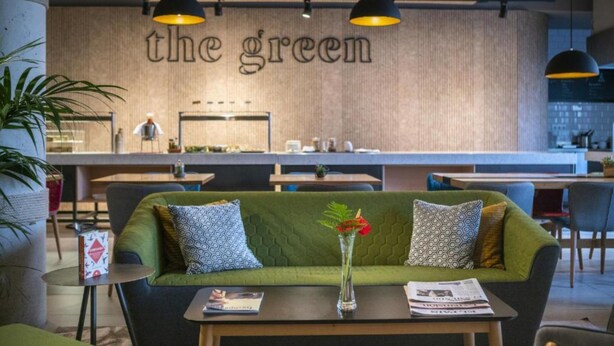 A modern cafe interior with a green sofa, a small table with a vase, and a wall with the text "the green". - ARTIEM Madrid Hotel (Madrid)