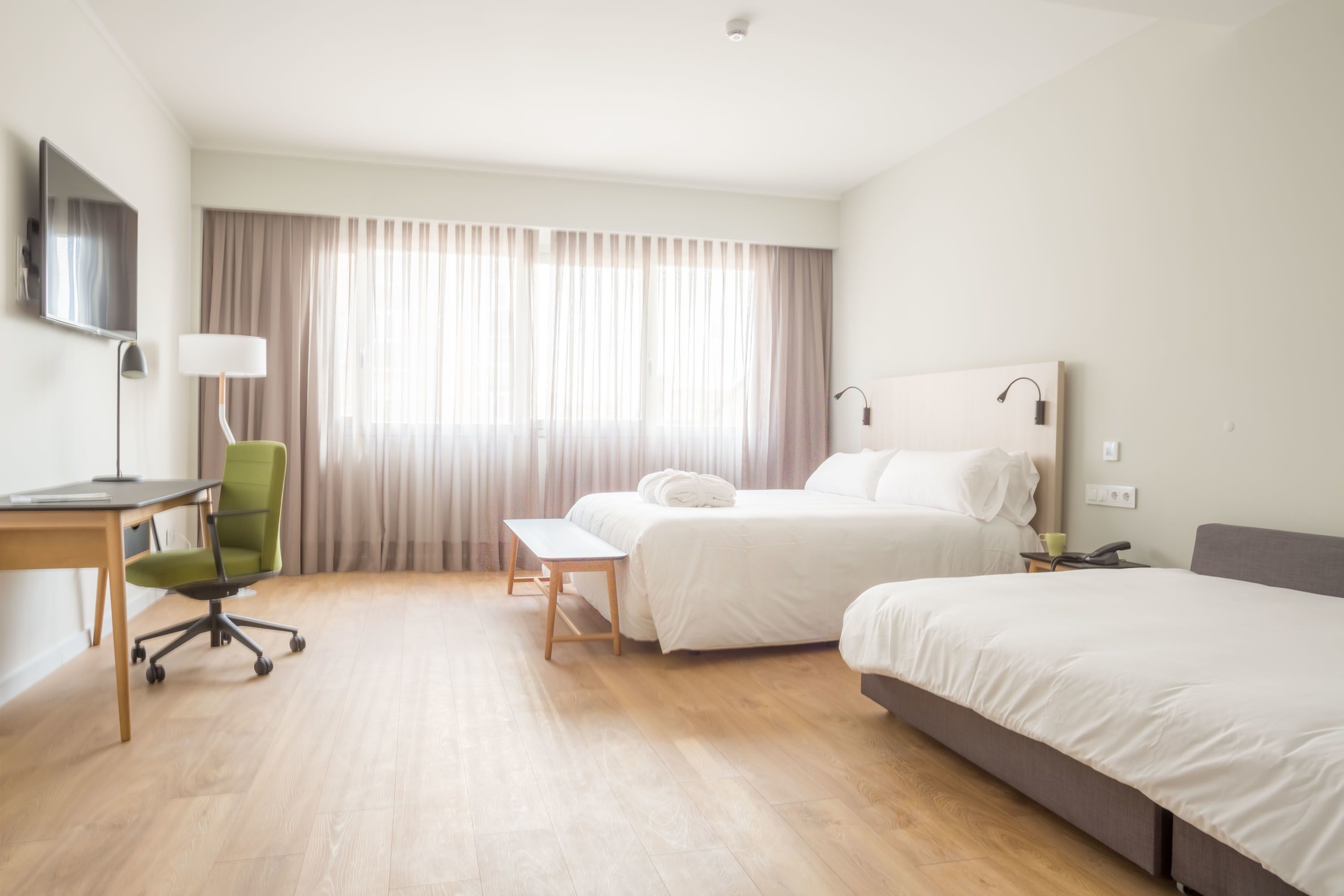 A hotel room with a bed, a desk, a chair, a lamp, and a TV.