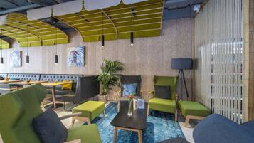 A modern lounge area with green upholstered seating, a coffee table, and a potted plant.