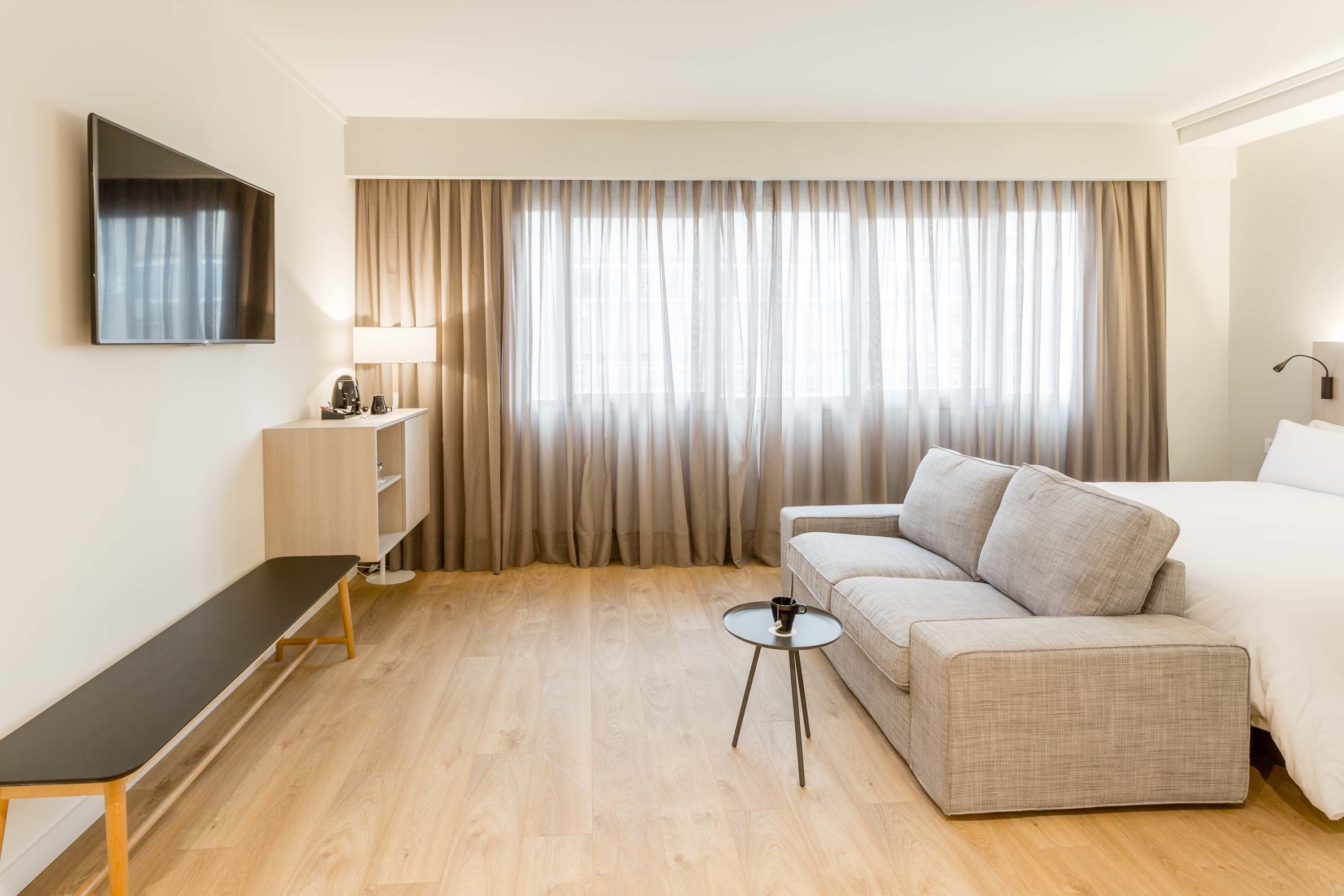 Una habitación de hotel con sofá, cama, televisor, una mesita y lámpara.