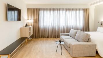 Una habitación de hotel con sofá, cama, televisor, una mesita y lámpara.