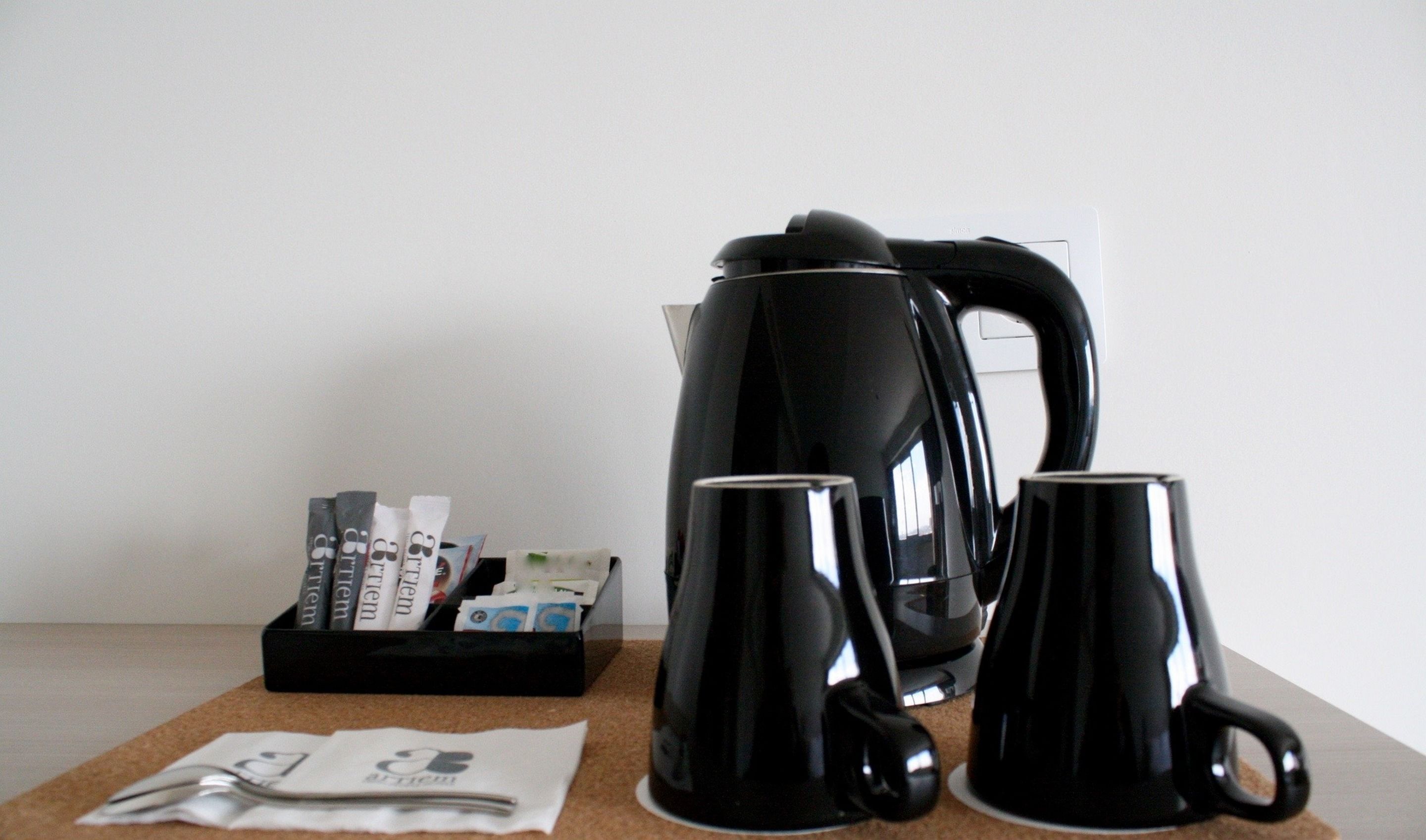 A coffee maker, two black mugs, a pair of scissors, and a box of coffee pods on a table.