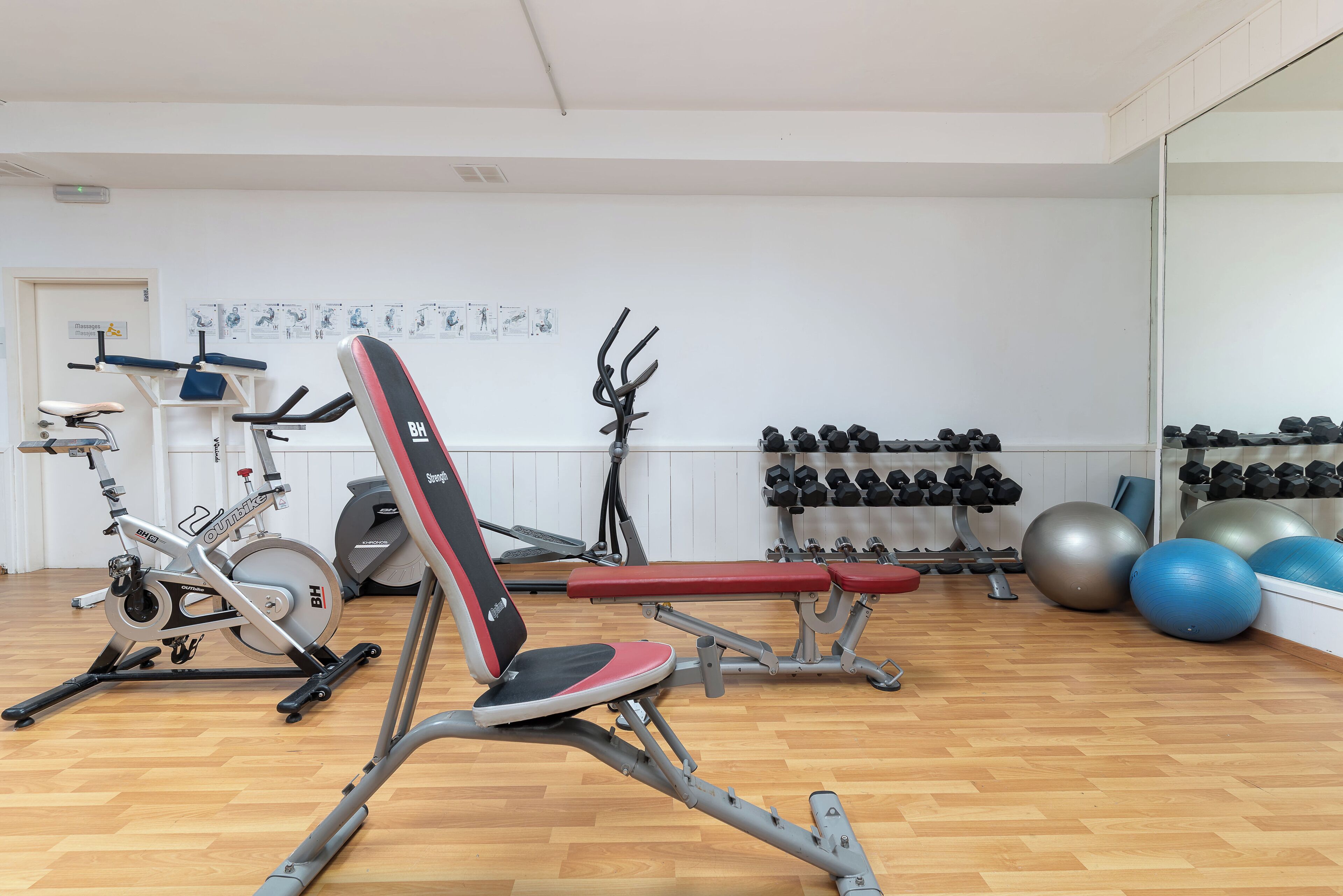 Une salle de sport équipée de machines d’exercice, de bancs et d’un mur rempli d’haltères.
