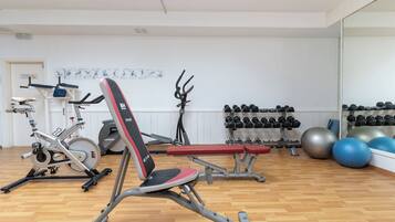 A gym with exercise equipment, benches, and a wall of dumbbells.