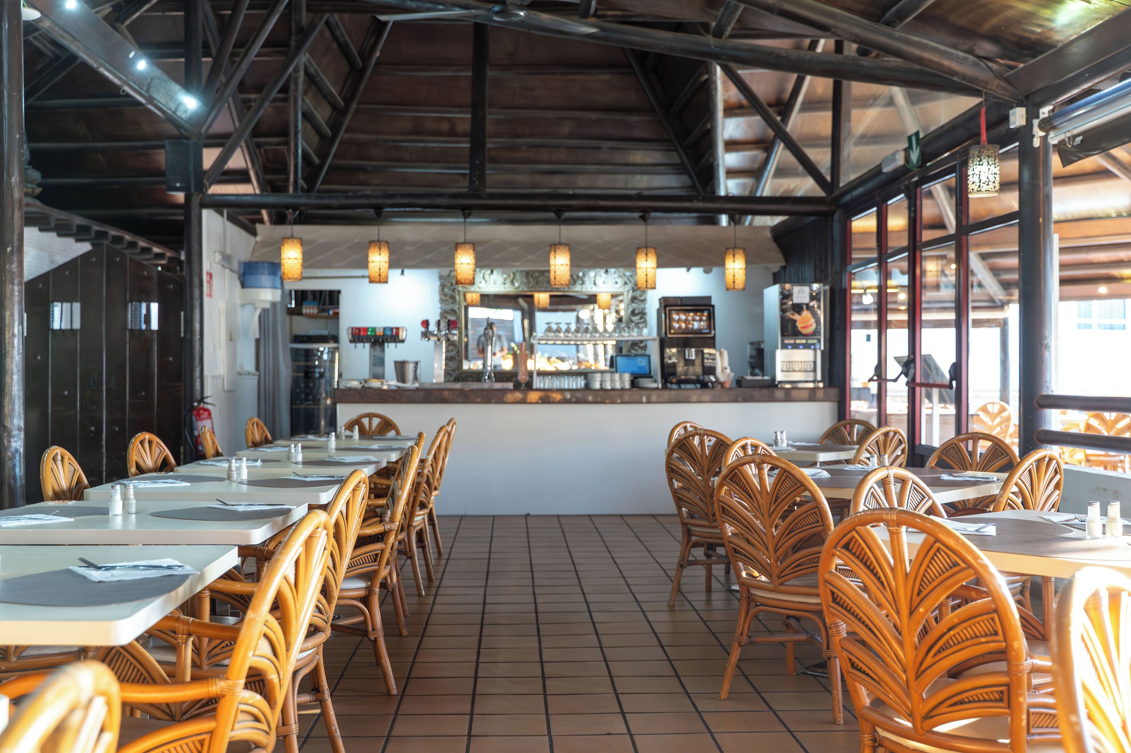 A restaurant with wooden chairs and tables, a counter with a display case, and hanging lights.