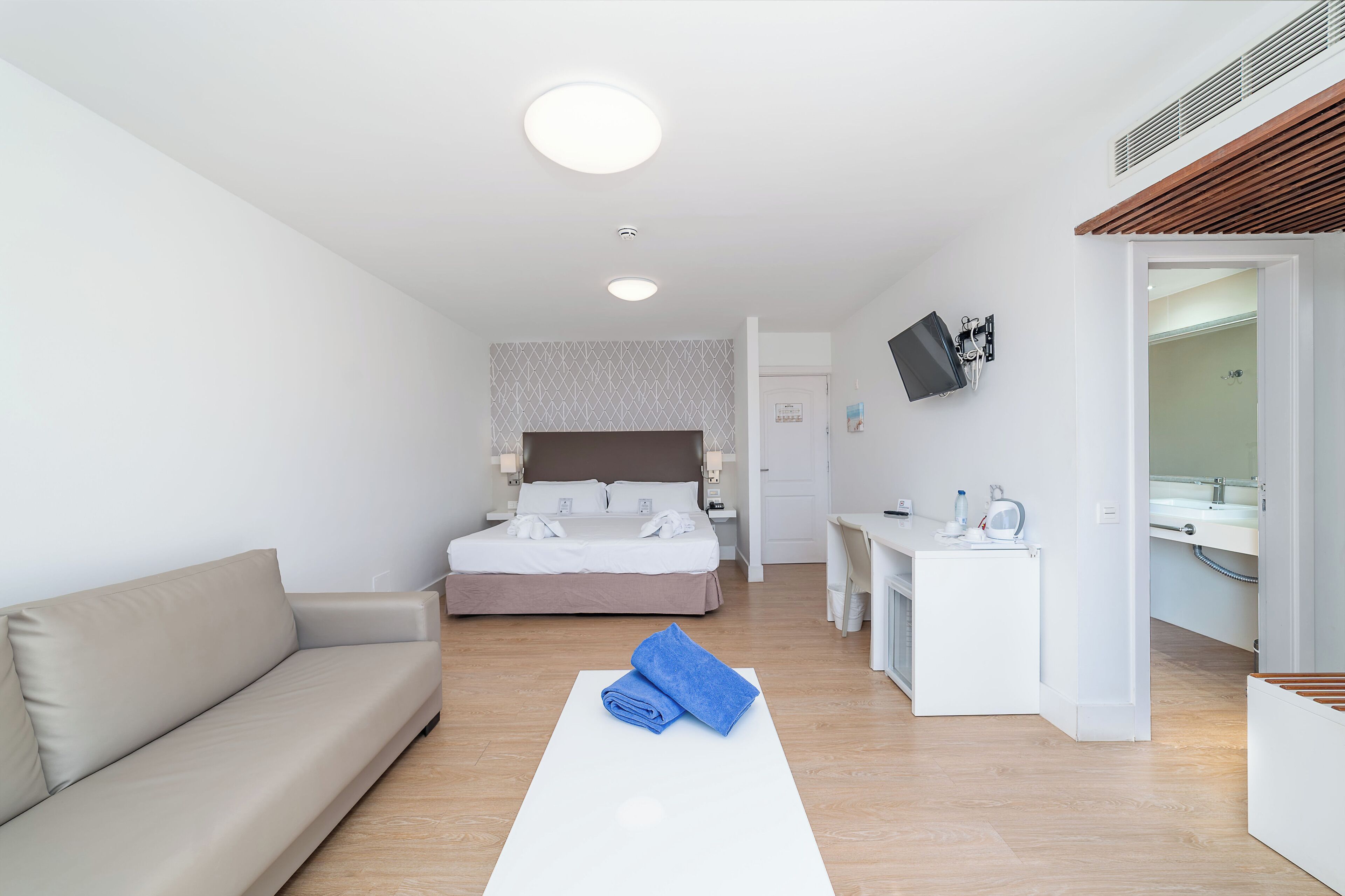 A hotel room with a bed, a sofa, a desk, and a bathroom.
