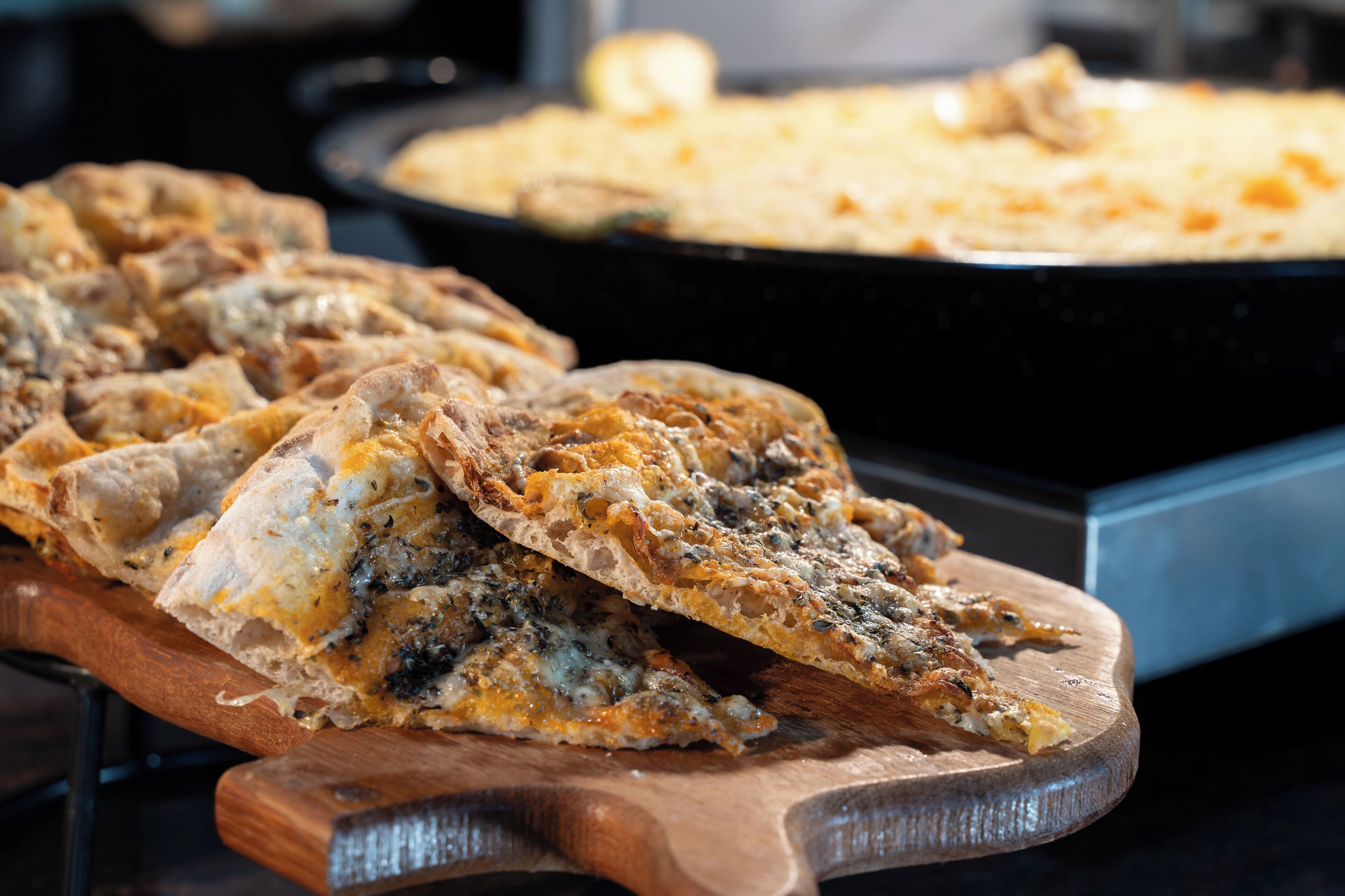 Een houten snijplank met plakjes platbrood belegd met kaas en kruiden.