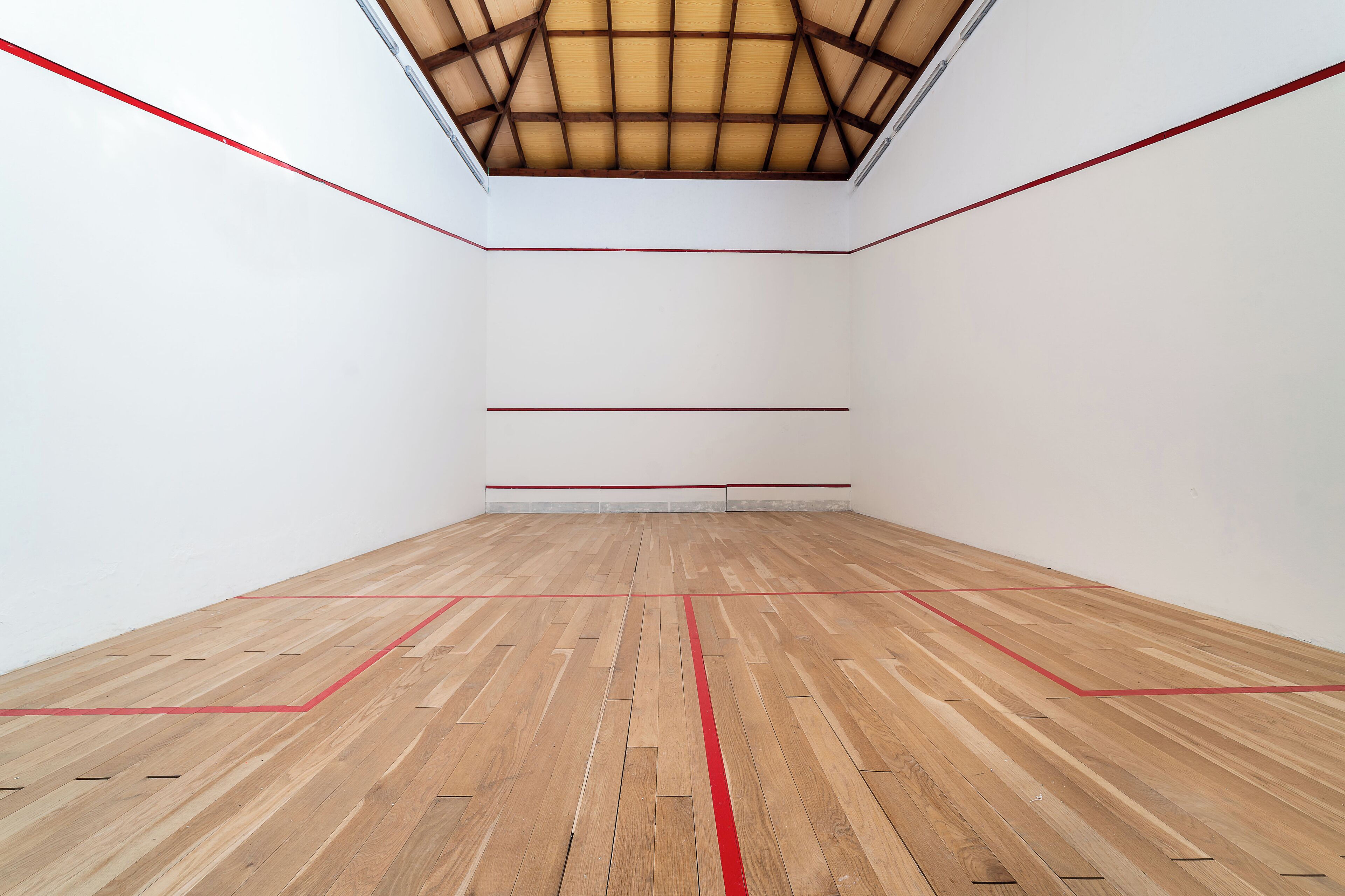 Una cancha de squash con suelo de madera y líneas delimitadoras rojas.