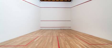 A squash court with wooden flooring and red boundary lines.