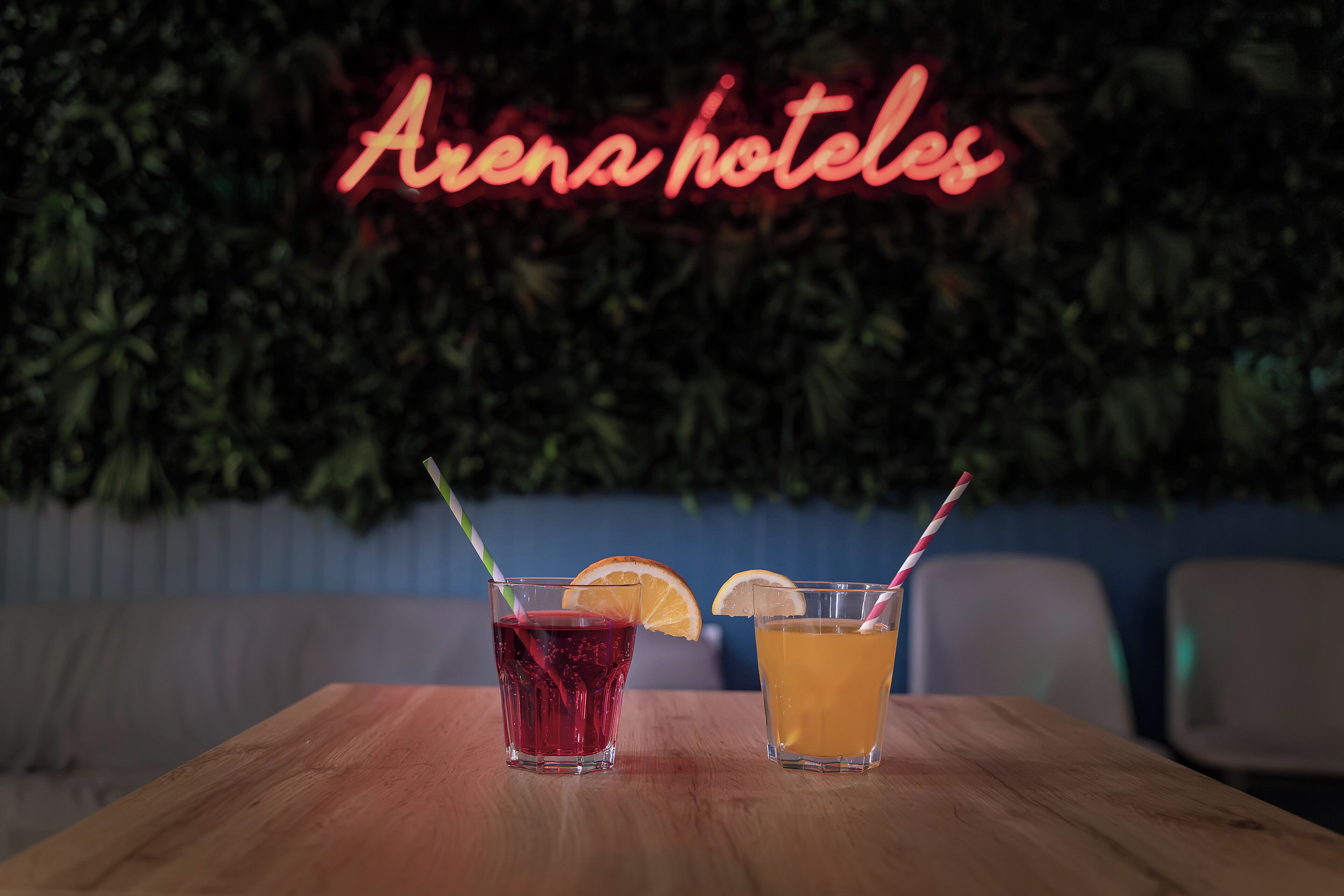 Two drinks on a wooden table with a neon sign reading "Arena hotels" in the background.