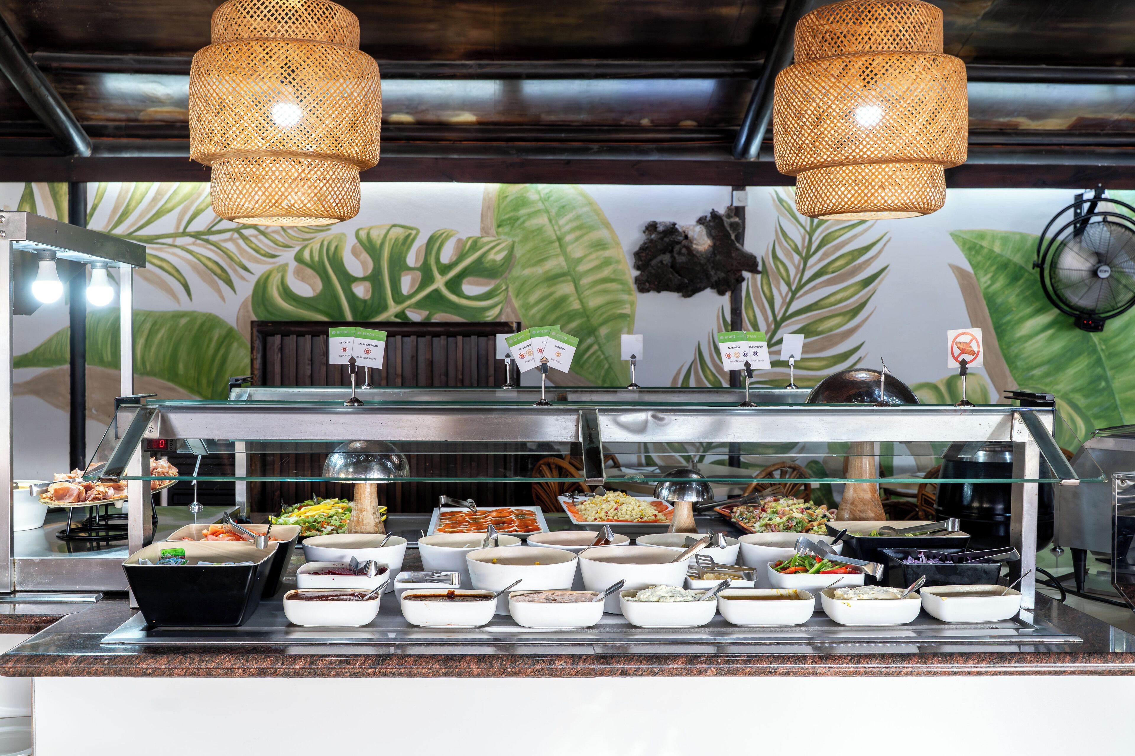 Un bufé con diversas opciones de comida y un mural tropical de fondo.