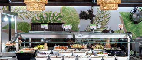 Un bufé con diversas opciones de comida y un mural tropical de fondo.