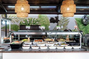 Un bufé con diversas opciones de comida y un mural tropical de fondo.