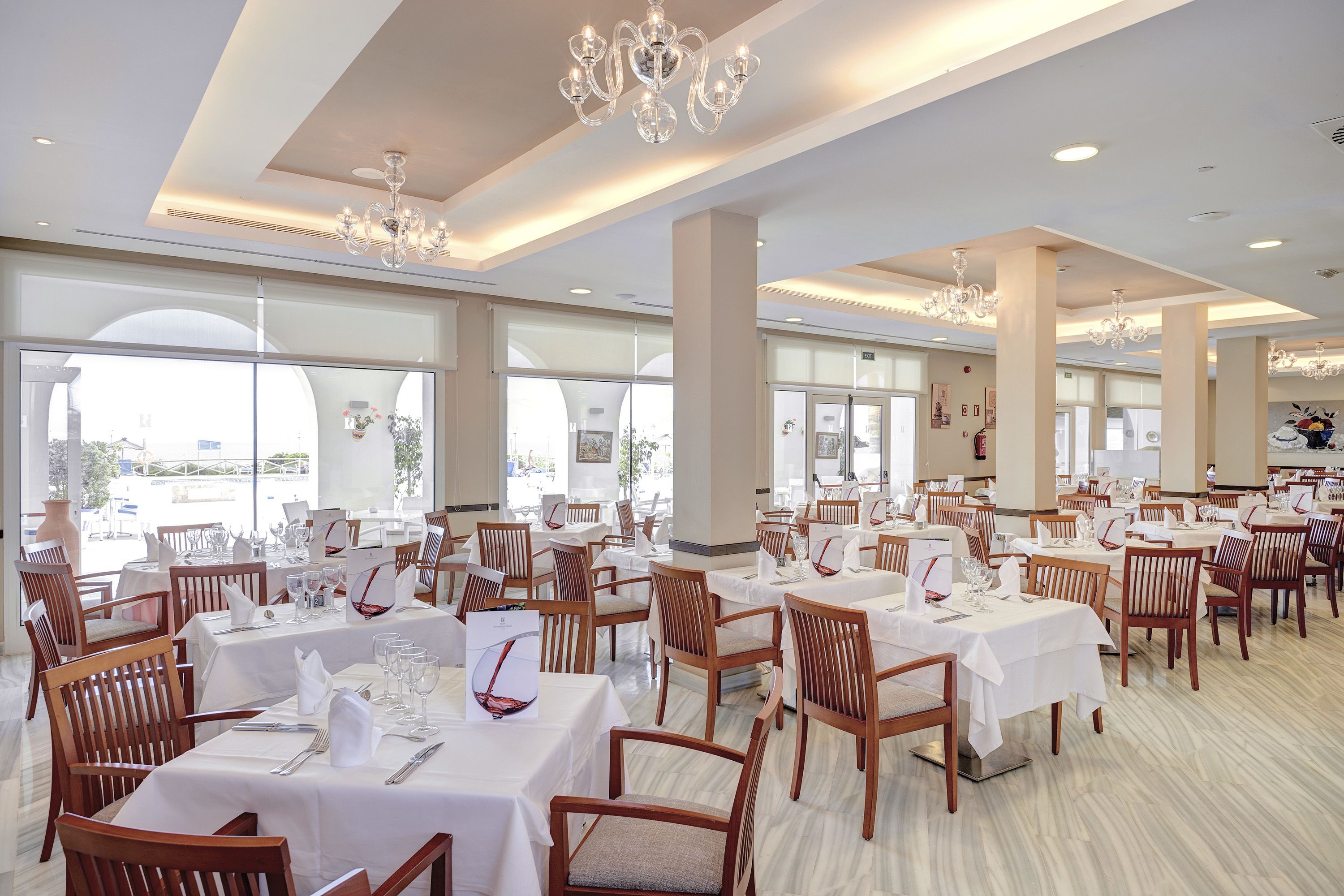 Un vaste espace dédié à la salle à manger, avec de nombreuses tables et chaises, de grandes fenêtres et des lustres.