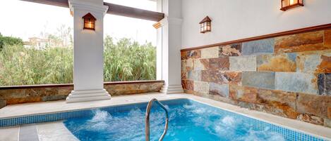Un jacuzzi con pared de piedra y columnas, vistas a la vegetación y dos faroles en la pared.