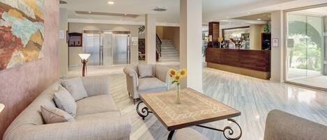 Un hall con un sofá, una mesa de centro con un jarrón y un mostrador de recepción.