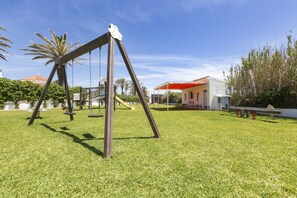 A playground with swings and a slide, surrounded by grass and trees. - Hipotels Hotel Flamenco Conil (Conil de la Frontera)