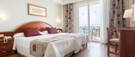 A hotel room with a large bed, a desk, a chair, and a balcony with curtains.