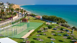 Een kustresort met een tennisbaan, loungezetels en parasols.