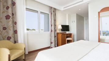 Una habitación de hotel con cama, una silla, escritorio con televisor y ventana con cortinas.