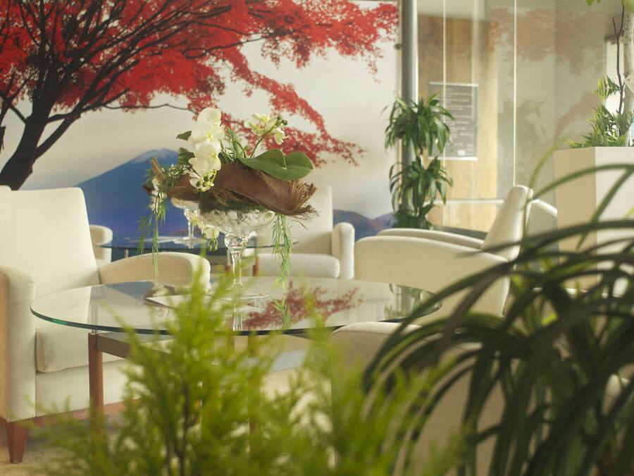 A modern living room with a glass coffee table, white sofas, and a large red tree mural on the wall.
