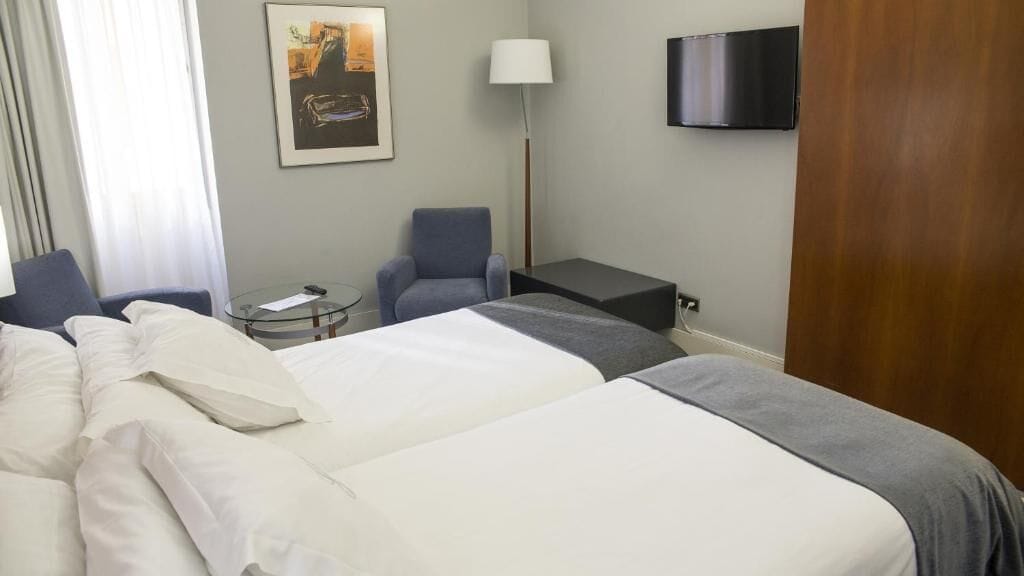 Ett hotellrum med två sängar, ett skrivbord, en stol, en tv och en tavla på väggen.