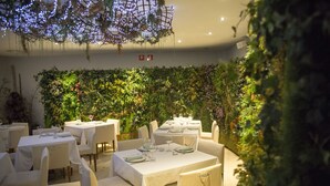 A restaurant with tables set for dining, a green wall with plants, and hanging lights. - Gran Hotel Albacete (Albacete)