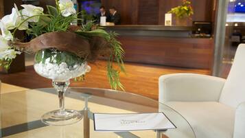 A reception area with a glass table, a vase with white flowers, and a reception desk in the background.