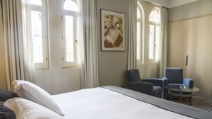 A hotel room with a large bed, two armchairs, a small table, and a painting on the wall. - Gran Hotel Albacete (Albacete)