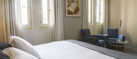 A hotel room with a large bed, two armchairs, a small table, and a painting on the wall.
