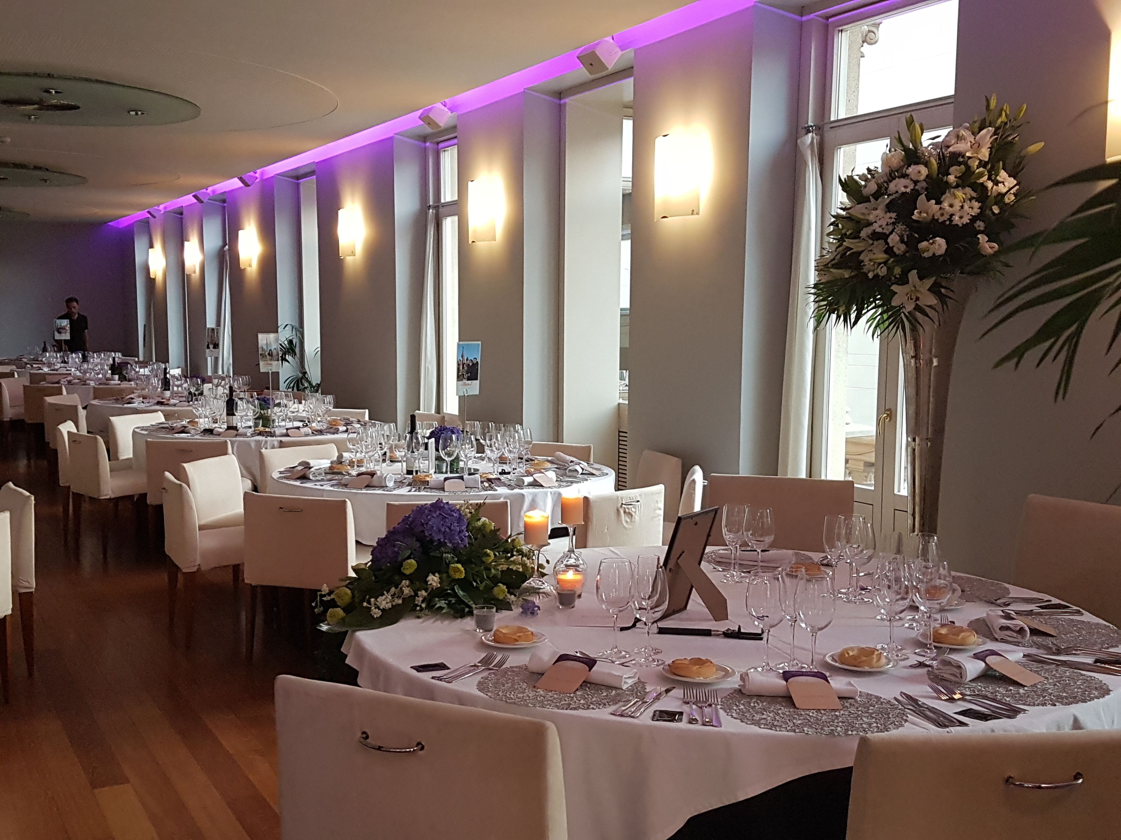 A banquet hall with round tables set for dining, featuring white tablecloths, silverware, and glassware.