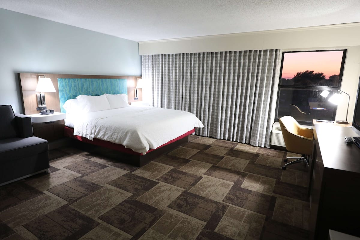 Habitación de hotel con cama, escritorio, silla, mesita de noche y ventana con cortinas.