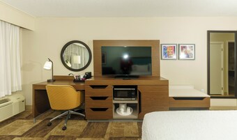 Quarto de hotel com escrivaninha de madeira, televisão, espelho, cadeira, micro-ondas e cama.