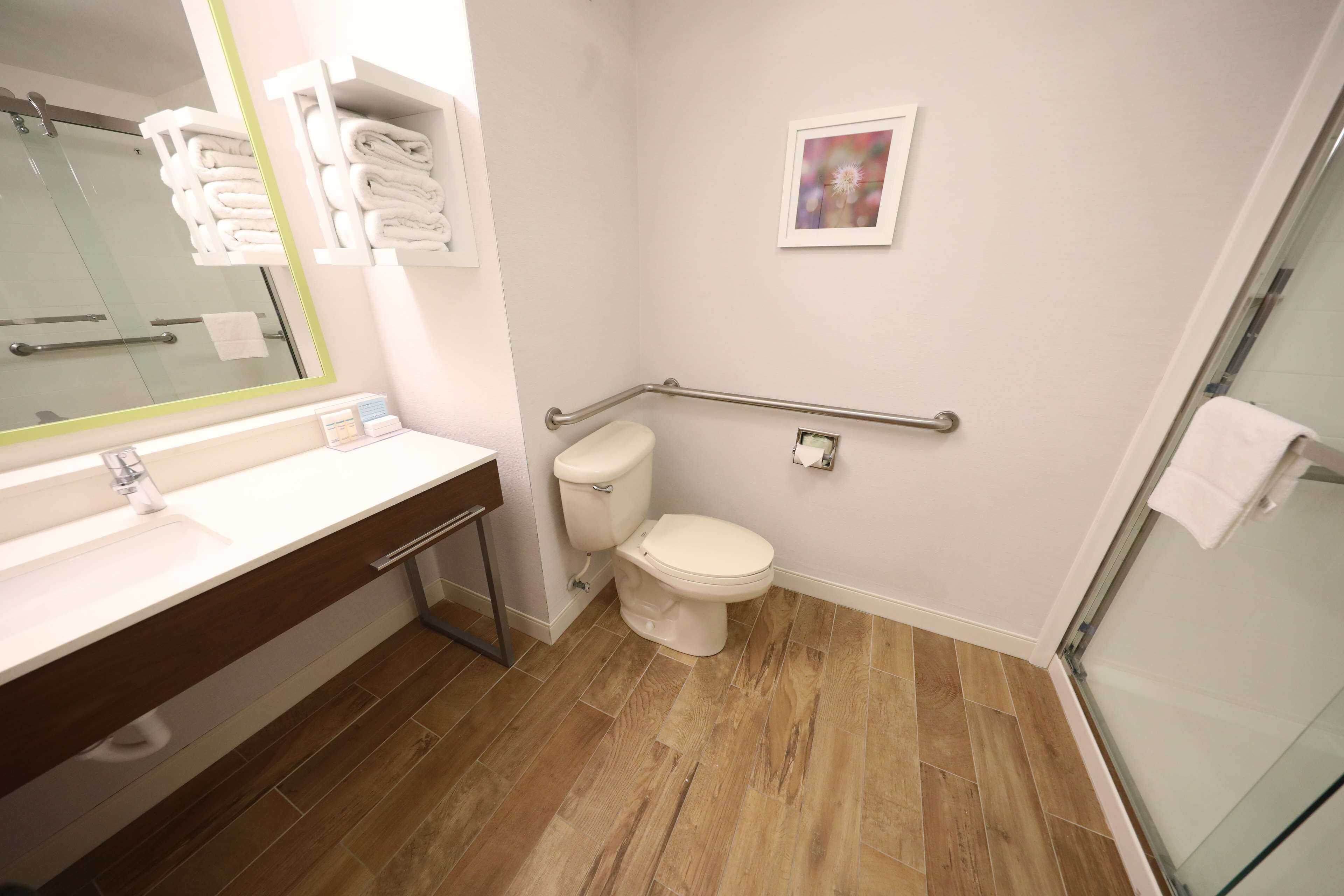 Un baño con lavamanos blanco, inodoro, cabina de ducha de vidrio y barandilla.