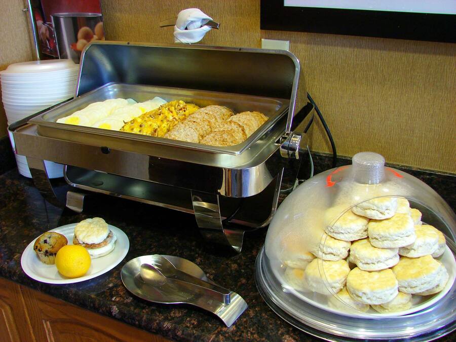 A buffet setup with various food items including biscuits, muffins, and a covered container of biscuits.
