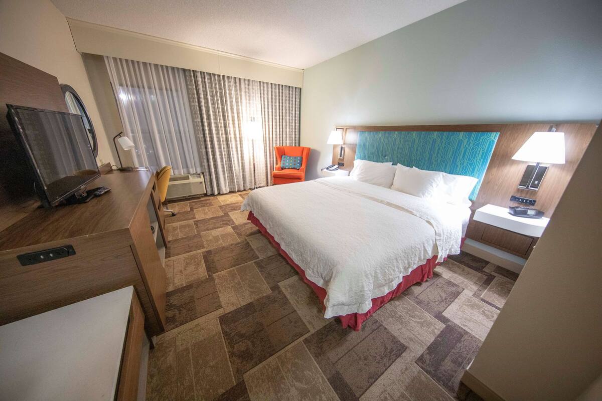 Una habitación de hotel con una cama grande, un escritorio, una silla, un televisor y una ventana con cortinas.