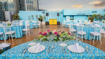 A rooftop event space with multiple round tables set for a formal event, featuring blue tablecloths and white chairs.