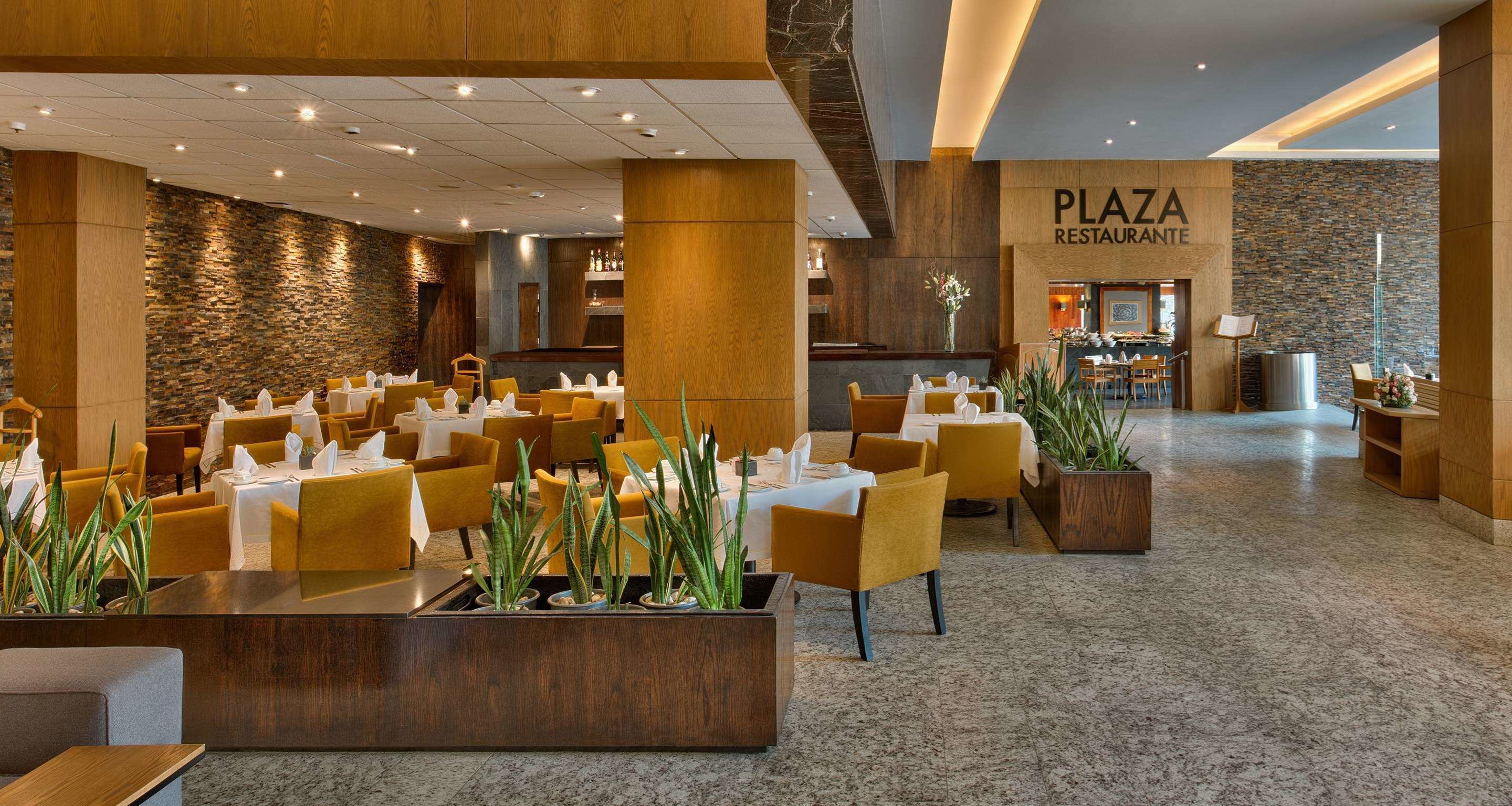 Eine großzügige Lobby mit mehreren Sitzbereichen, einem Empfangstresen und einem Restaurant namens 'Plaza Restaurante'.