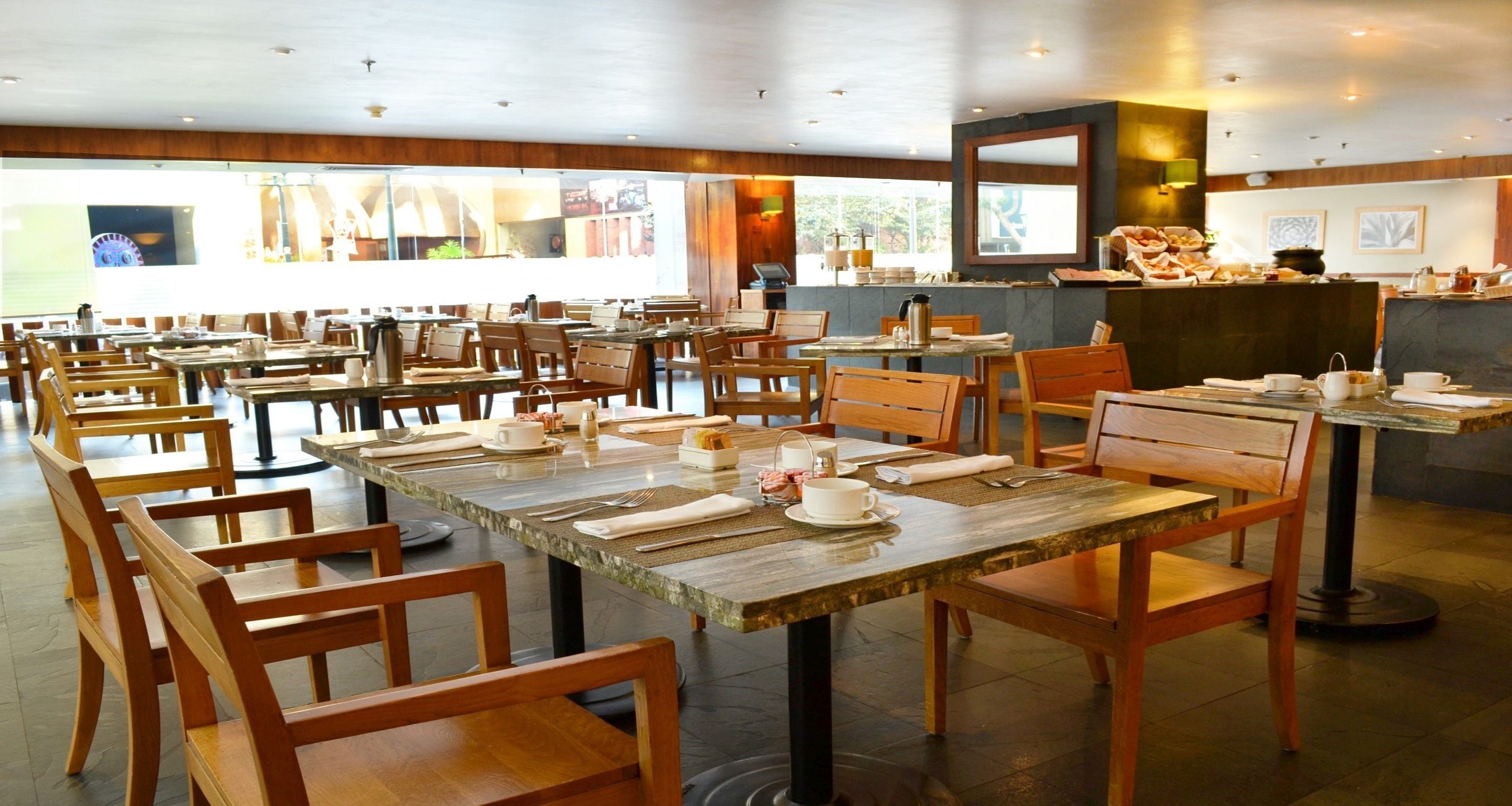 Un restaurante amplio con mesas y sillas de madera, una zona de bufé y un mostrador con comida y bebidas.