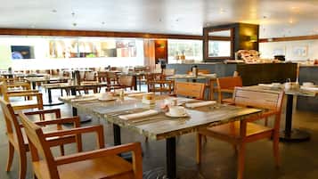 Un restaurante amplio con mesas y sillas de madera, una zona de bufé y un mostrador con comida y bebidas.