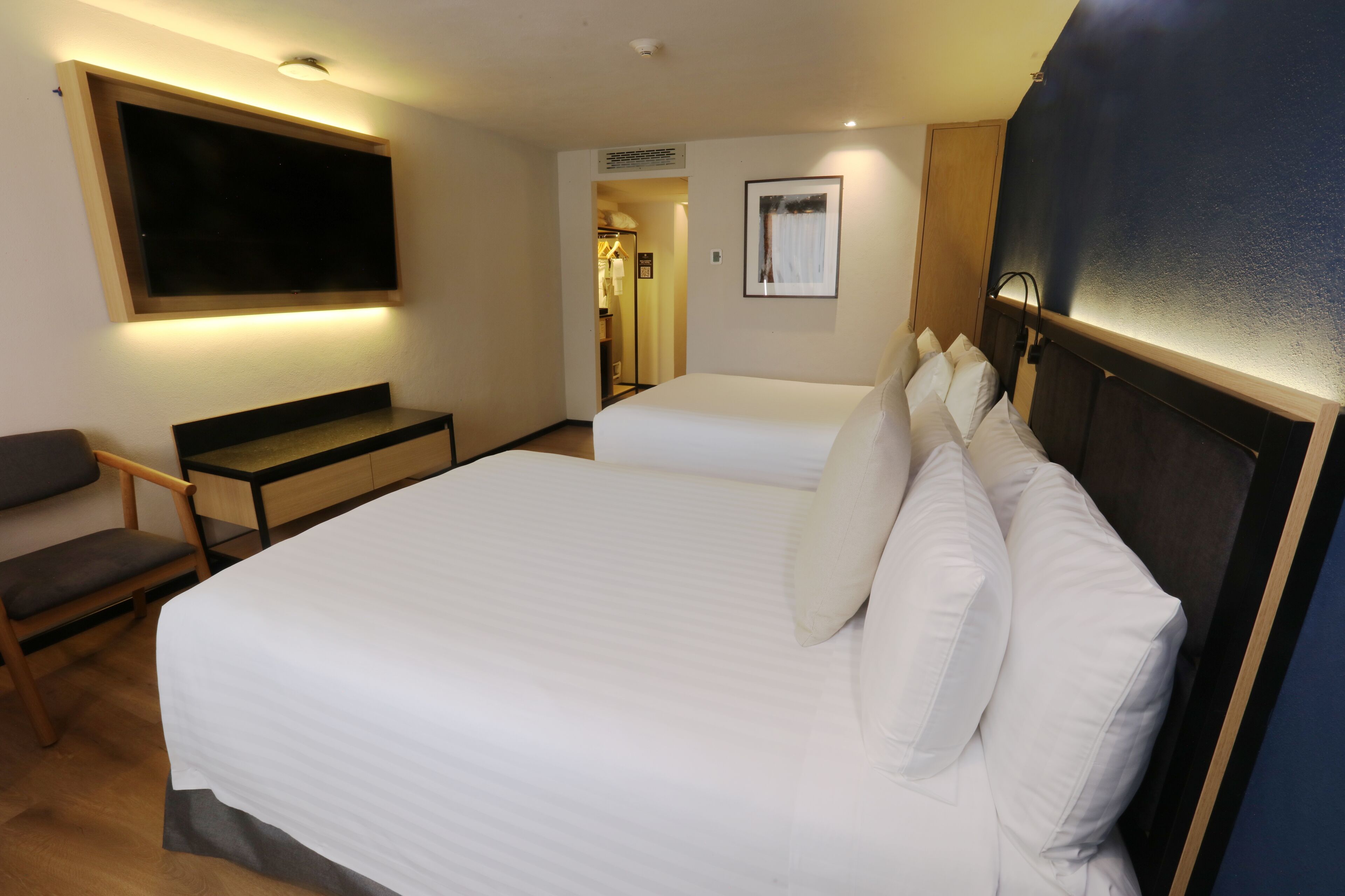 Une chambre d’hôtel avec un grand lit, un bureau, une chaise, un téléviseur fixé au mur et une porte donnant accès à une salle de bain.
